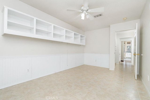 empty room featuring a wainscoted wall, visible vents, and a ceiling fan