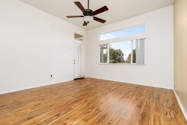 spare room with wood finished floors, a ceiling fan, and baseboards