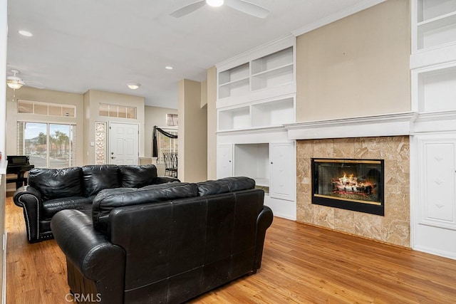 living area featuring ceiling fan, light wood-style floors, a tile fireplace, and built in features