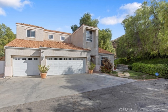 mediterranean / spanish-style house featuring driveway, an attached garage, a tiled roof, and stucco siding