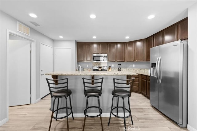 kitchen featuring dark brown cabinetry, visible vents, appliances with stainless steel finishes, a breakfast bar, and light wood-type flooring