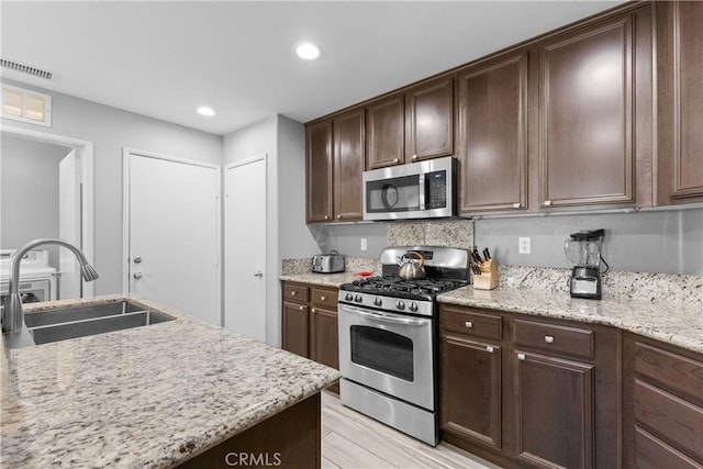 kitchen featuring stainless steel appliances, visible vents, a sink, dark brown cabinetry, and light stone countertops