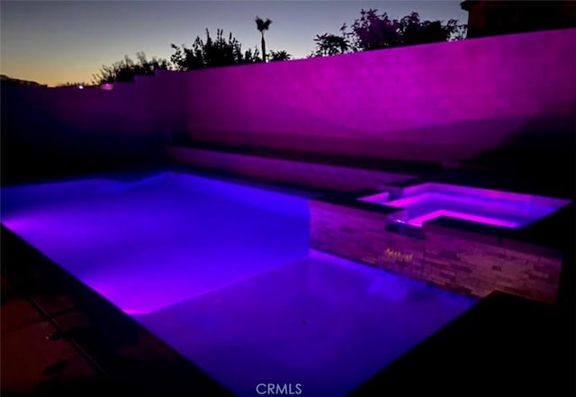 pool at dusk with a fenced backyard and a pool with connected hot tub