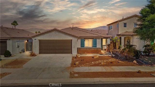 mediterranean / spanish house featuring a garage, driveway, a tiled roof, and stucco siding