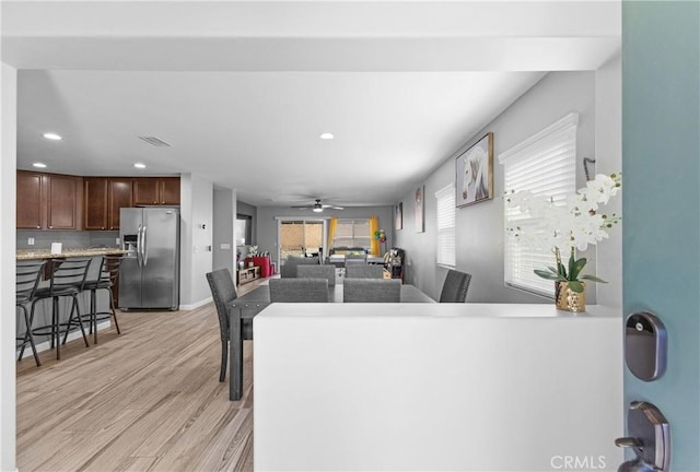 kitchen with a healthy amount of sunlight, light wood finished floors, stainless steel refrigerator with ice dispenser, and a kitchen breakfast bar