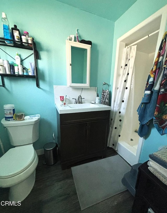 bathroom with baseboards, toilet, wood finished floors, vanity, and a shower stall