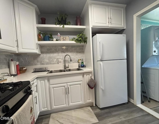 kitchen featuring gas range oven, decorative backsplash, freestanding refrigerator, white cabinetry, and a sink