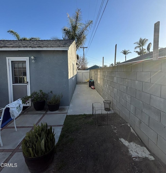 view of side of home featuring roof with shingles, fence, a patio, and stucco siding