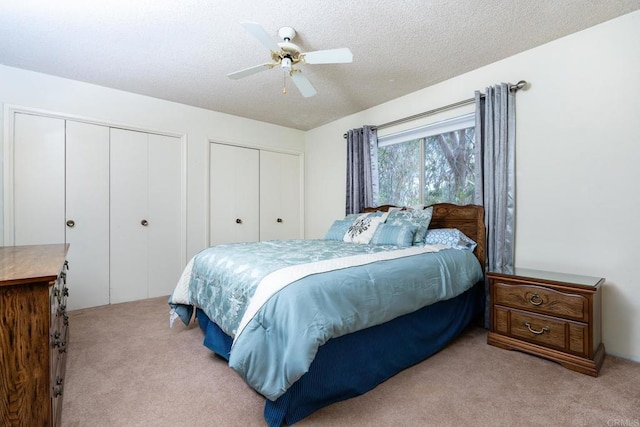 bedroom with carpet flooring, ceiling fan, a textured ceiling, and two closets