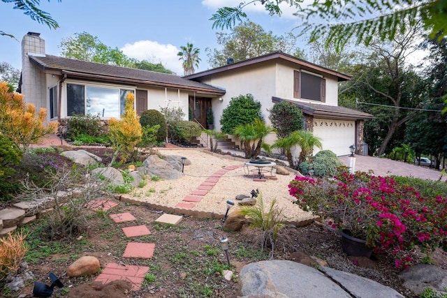 view of front of home with a garage, driveway, a chimney, and stucco siding