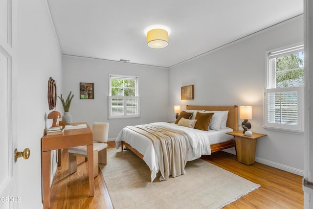 bedroom with visible vents, baseboards, light wood-style floors, and ornamental molding