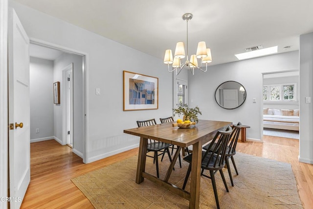 dining space with an inviting chandelier, light wood-style floors, visible vents, and baseboards