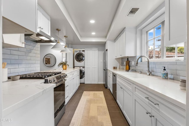 kitchen featuring visible vents, a sink, appliances with stainless steel finishes, white cabinets, and stacked washer / drying machine