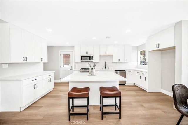 kitchen featuring light wood finished floors, backsplash, appliances with stainless steel finishes, a sink, and a kitchen bar