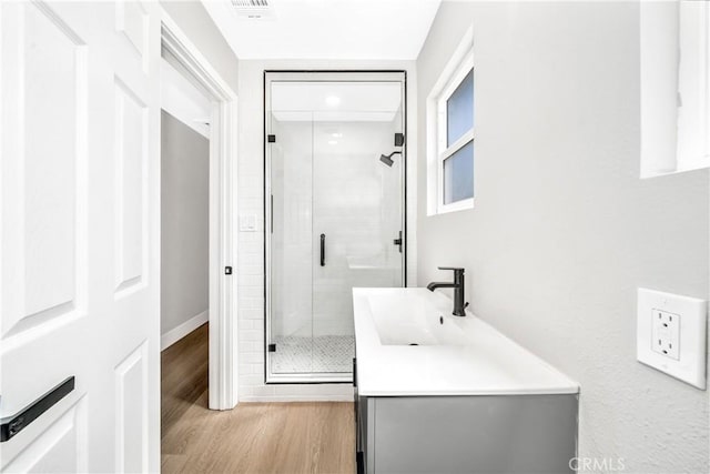 full bath with visible vents, a stall shower, vanity, wood finished floors, and baseboards