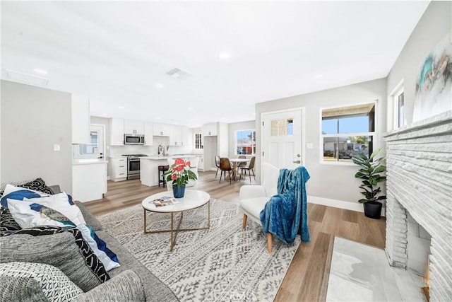 living room featuring baseboards, a brick fireplace, recessed lighting, and light wood-style floors