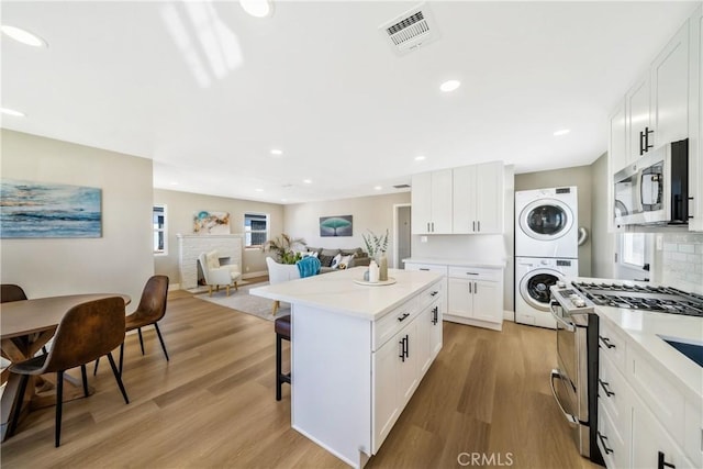 kitchen featuring stacked washer and dryer, visible vents, appliances with stainless steel finishes, a center island, and light wood-type flooring