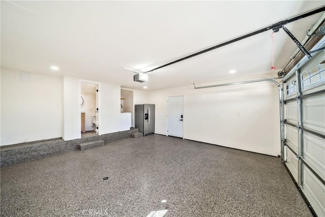 garage featuring a garage door opener and stainless steel refrigerator with ice dispenser