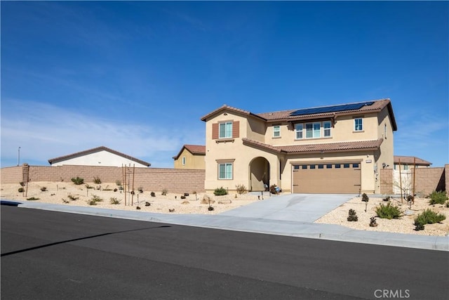 mediterranean / spanish-style home with stucco siding, driveway, roof mounted solar panels, fence, and a tiled roof