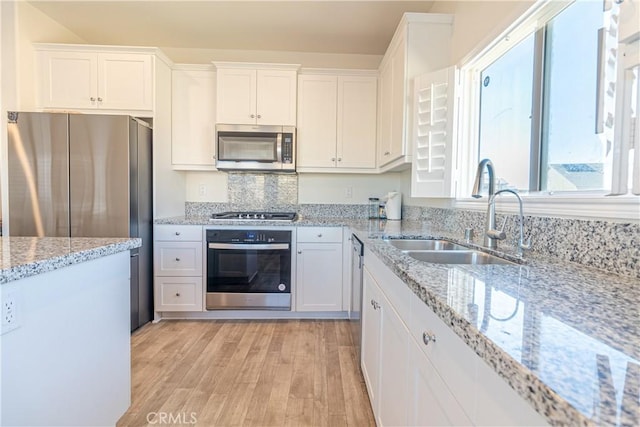 kitchen featuring a sink, white cabinetry, appliances with stainless steel finishes, light wood finished floors, and light stone countertops