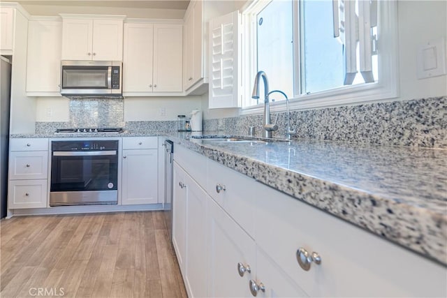 kitchen with light wood-type flooring, light stone counters, appliances with stainless steel finishes, white cabinetry, and a sink