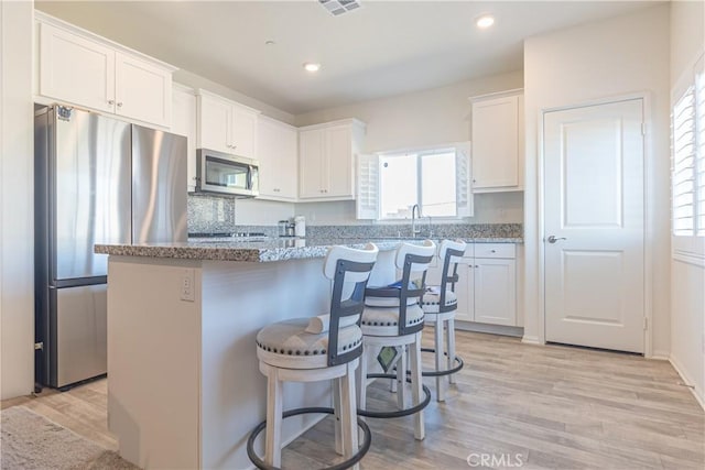 kitchen with white cabinetry, light stone countertops, appliances with stainless steel finishes, and a breakfast bar