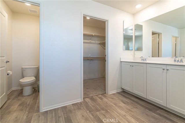 bathroom featuring wood finished floors, visible vents, double vanity, a sink, and toilet