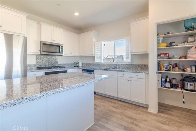 kitchen featuring light stone counters, a sink, white cabinets, light wood-style floors, and appliances with stainless steel finishes