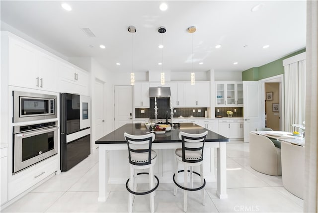 kitchen with dark countertops, under cabinet range hood, light tile patterned floors, and appliances with stainless steel finishes