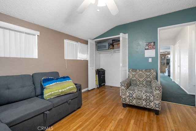 living area with hardwood / wood-style flooring, vaulted ceiling, a ceiling fan, and a textured ceiling