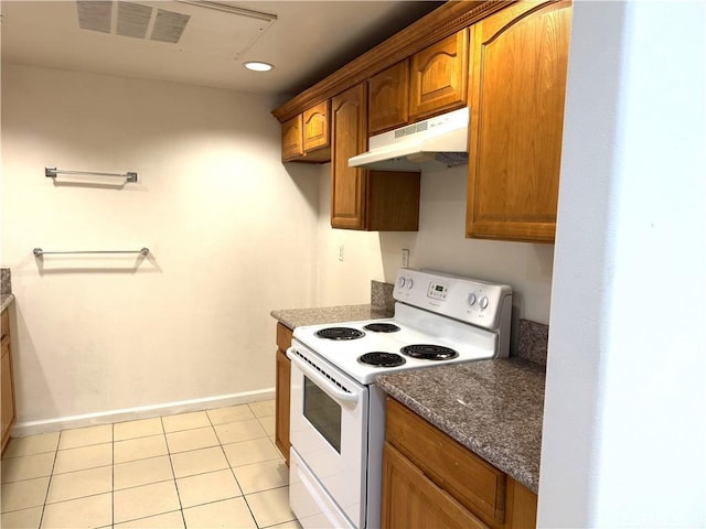 kitchen with white electric stove, light tile patterned floors, under cabinet range hood, baseboards, and dark stone countertops