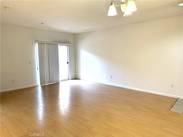 spare room with light wood-type flooring, baseboards, and a notable chandelier