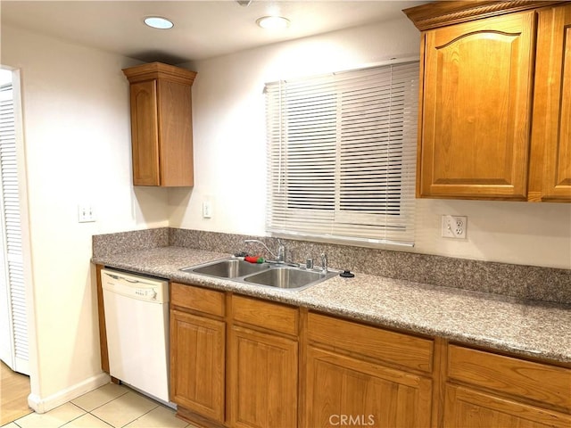 kitchen with light tile patterned floors, brown cabinetry, white dishwasher, and a sink