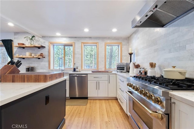 kitchen featuring stainless steel appliances, light stone countertops, white cabinetry, and exhaust hood