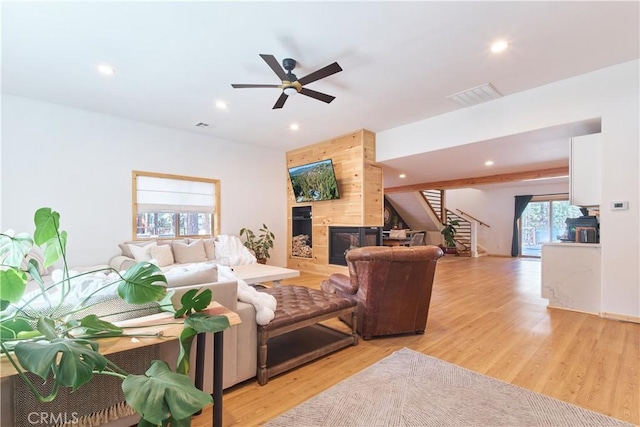 living room featuring visible vents, a tiled fireplace, stairs, light wood-style floors, and recessed lighting