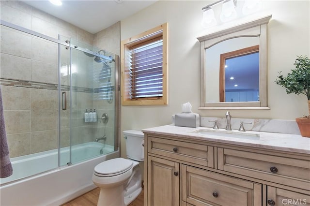 bathroom featuring toilet, enclosed tub / shower combo, wood finished floors, and vanity