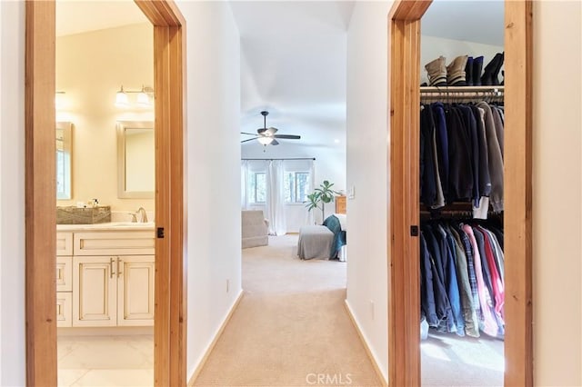 hallway featuring light colored carpet, a sink, and baseboards