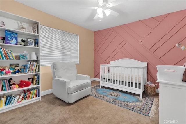 bedroom with ceiling fan, an accent wall, carpet flooring, baseboards, and a crib