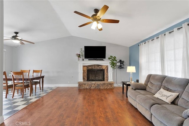 living room with lofted ceiling, a stone fireplace, wood finished floors, a ceiling fan, and baseboards