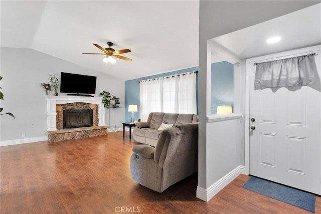 living room featuring a ceiling fan, vaulted ceiling, a stone fireplace, wood finished floors, and baseboards