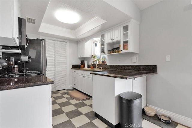 kitchen with a tray ceiling, crown molding, light floors, white cabinetry, and a sink