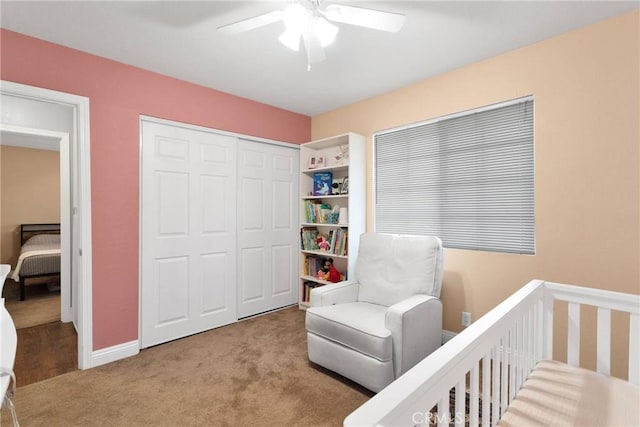 carpeted bedroom with a ceiling fan, a closet, a crib, and baseboards