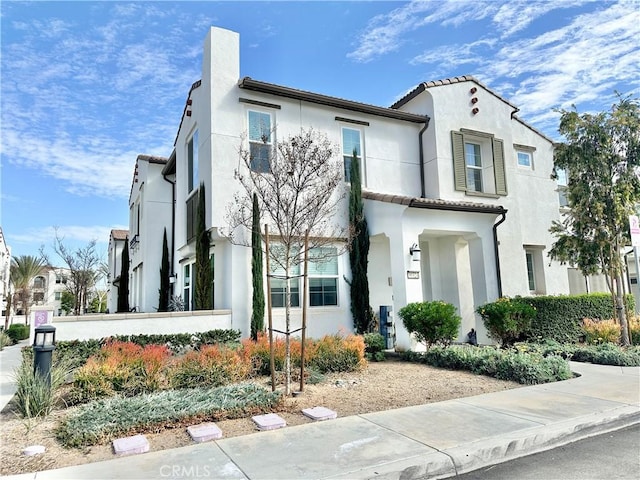 mediterranean / spanish home featuring a tiled roof, a chimney, and stucco siding