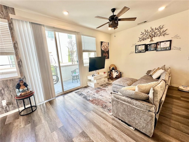 living area featuring a ceiling fan, visible vents, baseboards, and wood finished floors