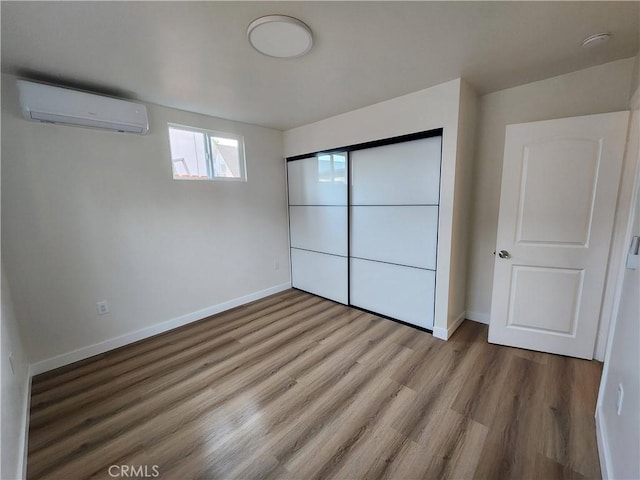 unfurnished bedroom with a wall mounted AC, wood finished floors, and baseboards