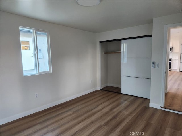 unfurnished bedroom featuring a closet, white fridge, wood finished floors, and baseboards