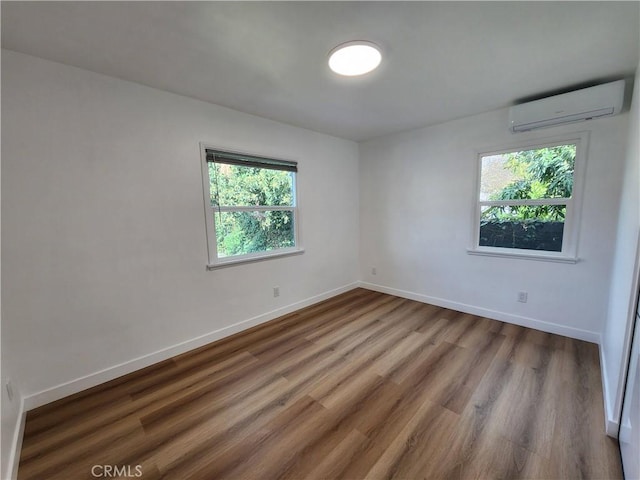 spare room with a wall mounted air conditioner, wood finished floors, and baseboards