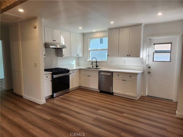 kitchen with dark wood finished floors, stainless steel appliances, light countertops, a sink, and under cabinet range hood