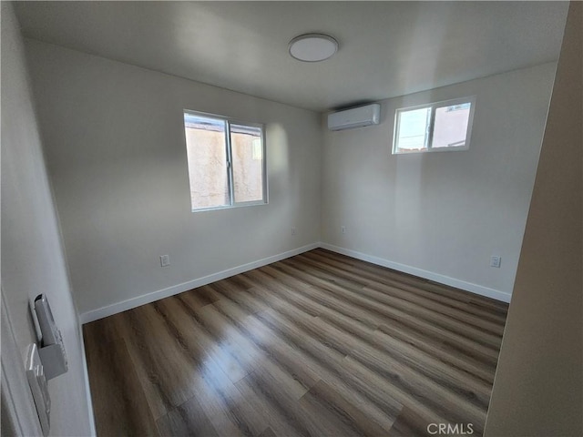 unfurnished room featuring a wealth of natural light, a wall unit AC, baseboards, and wood finished floors