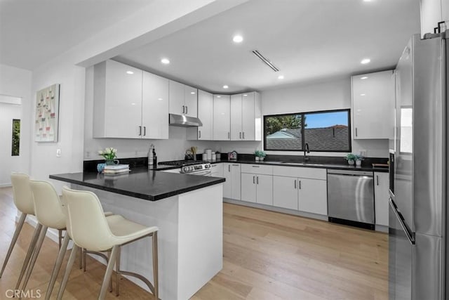 kitchen with under cabinet range hood, stainless steel appliances, a peninsula, a sink, and white cabinetry